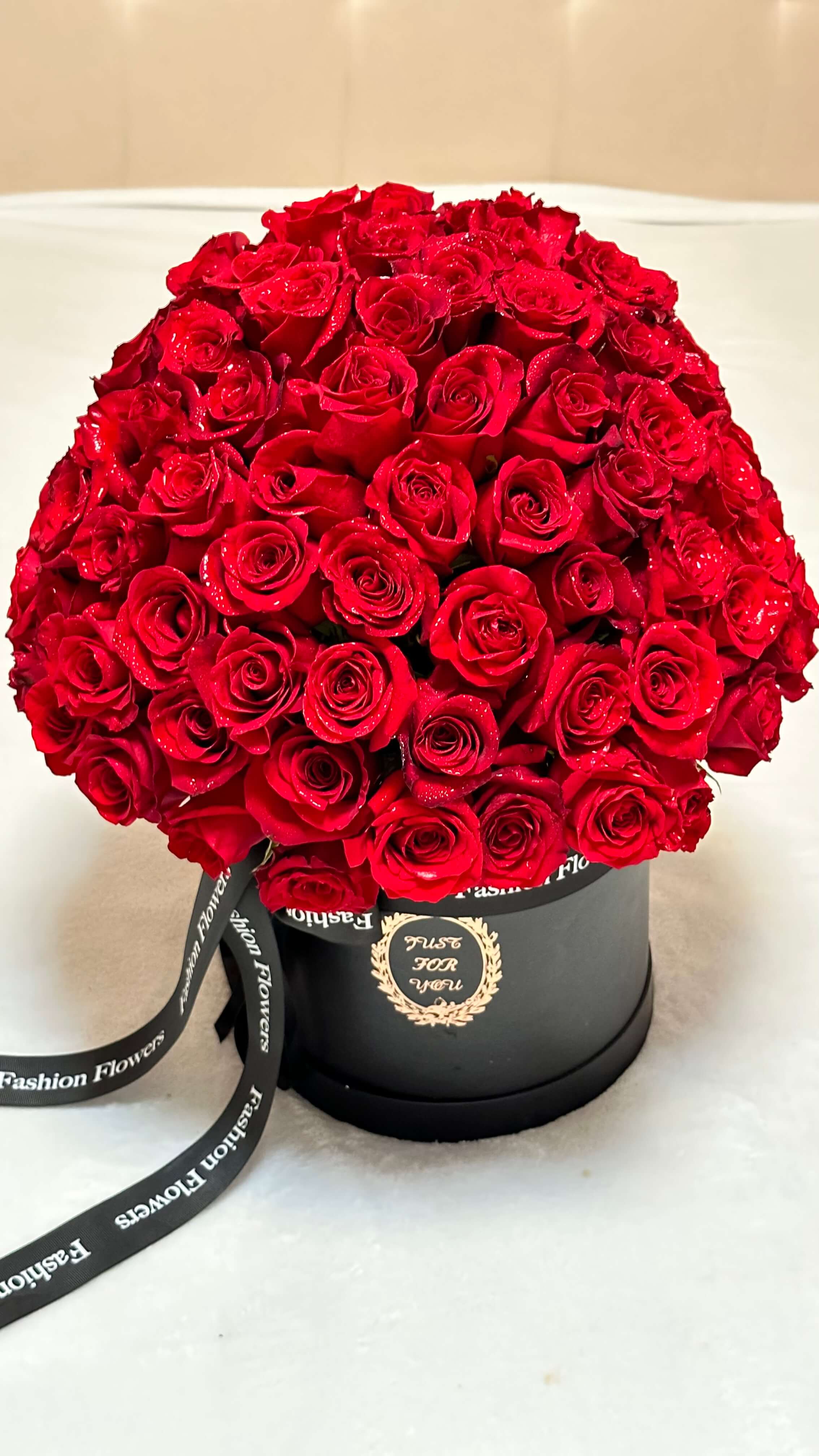 A stylish African American woman in a cream room with a designer box of red roses â classic elegance.