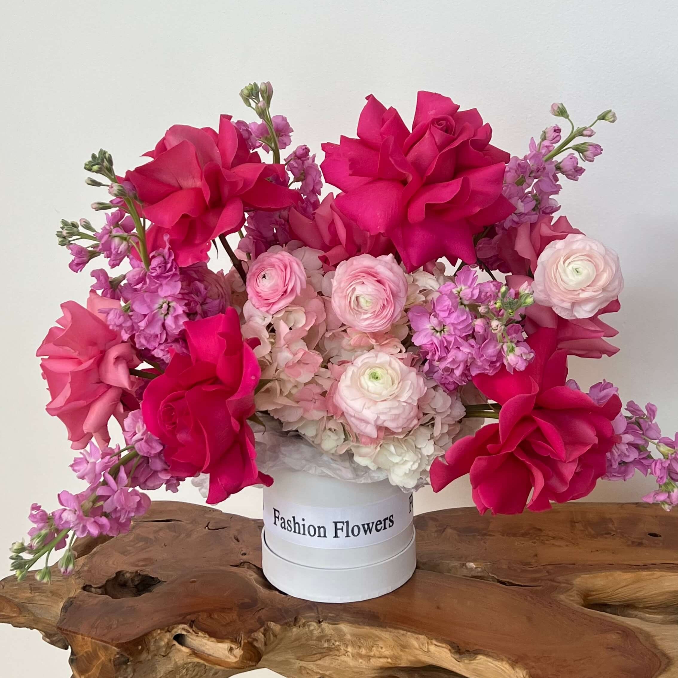 Luxury box bouquet with hot pink and blush flowers held by smiling woman in cozy elegant interior