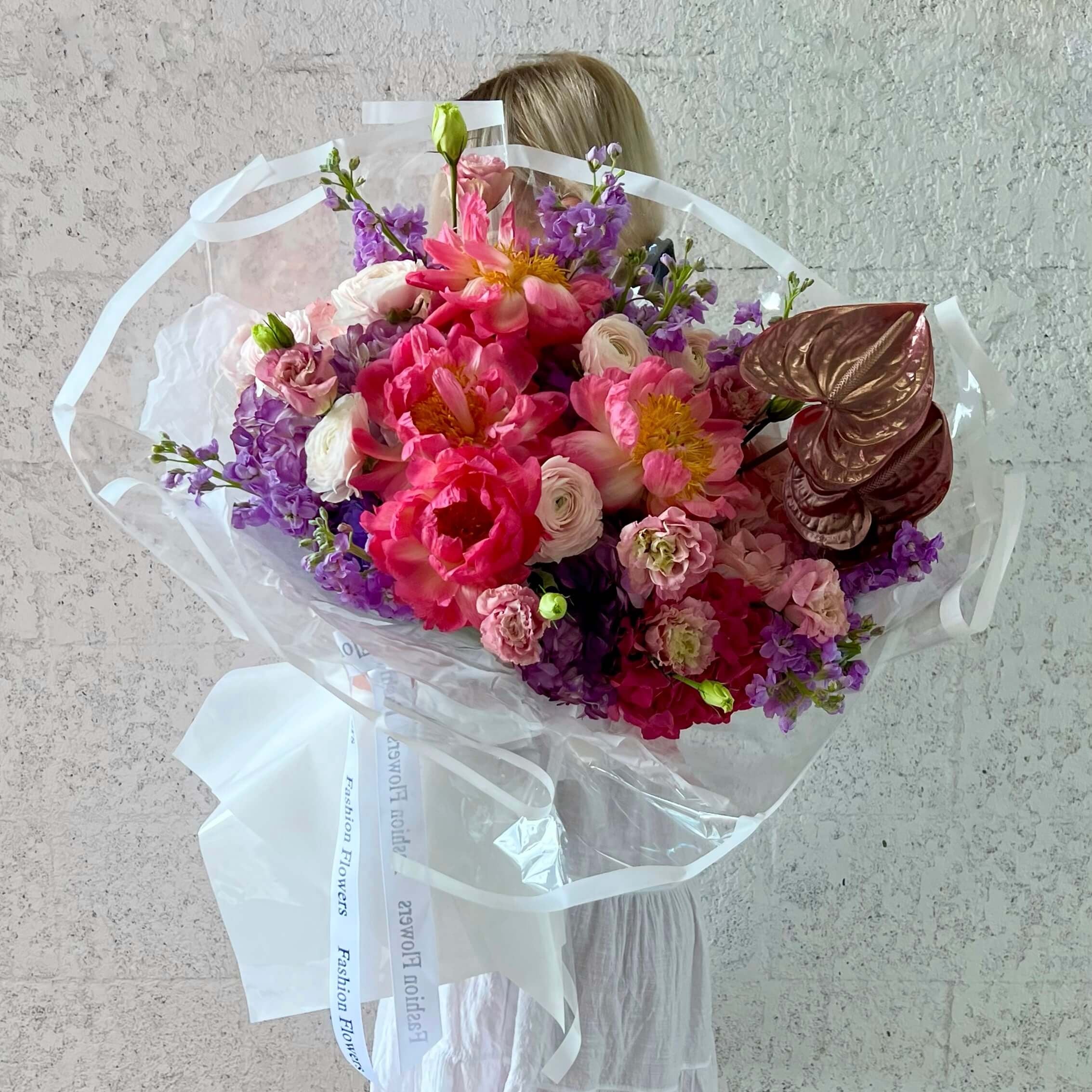 Monika bouquet of vibrant pink peonies and pastel flowers in transparent wrap held by elegant woman in villa