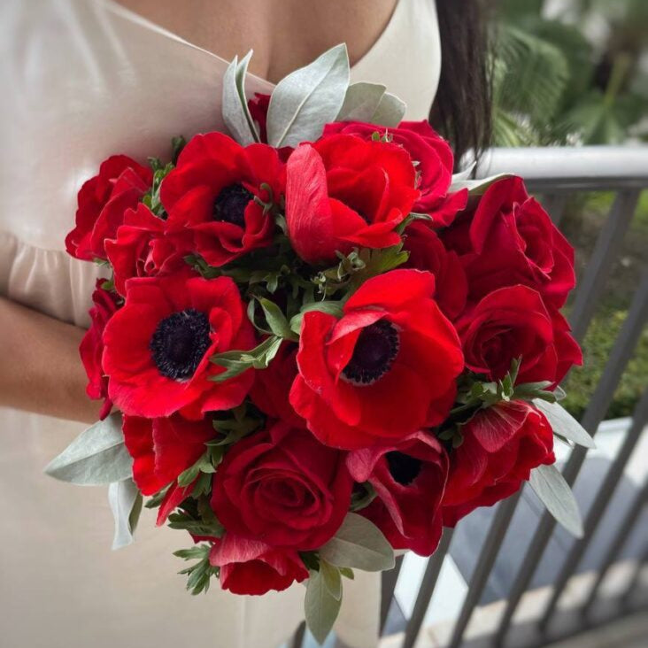 ne Love bouquet of red roses and anemones with silver leaves held by elegant woman on balcony — romantic gift Miami