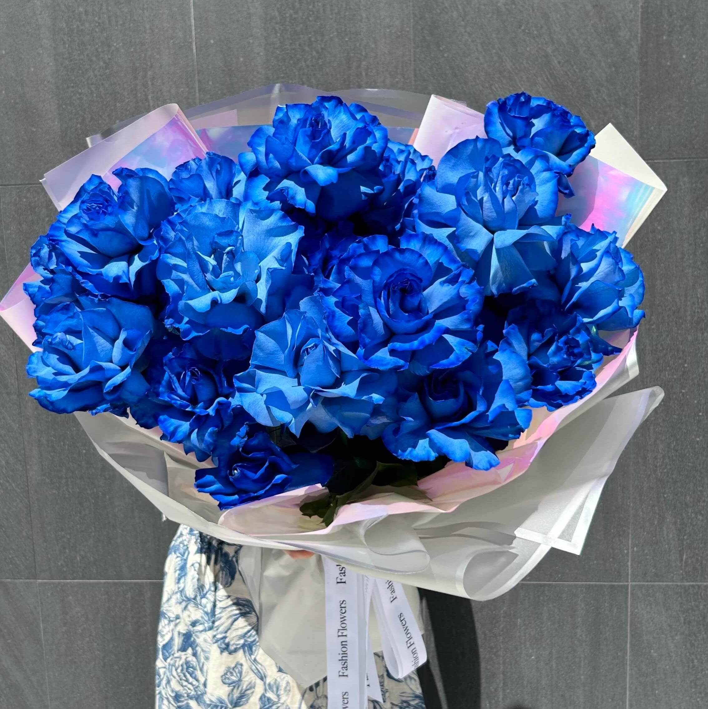 Vibrant bouquet of open blue roses wrapped in iridescent silver and sheer white paper — luxury Miami flower delivery