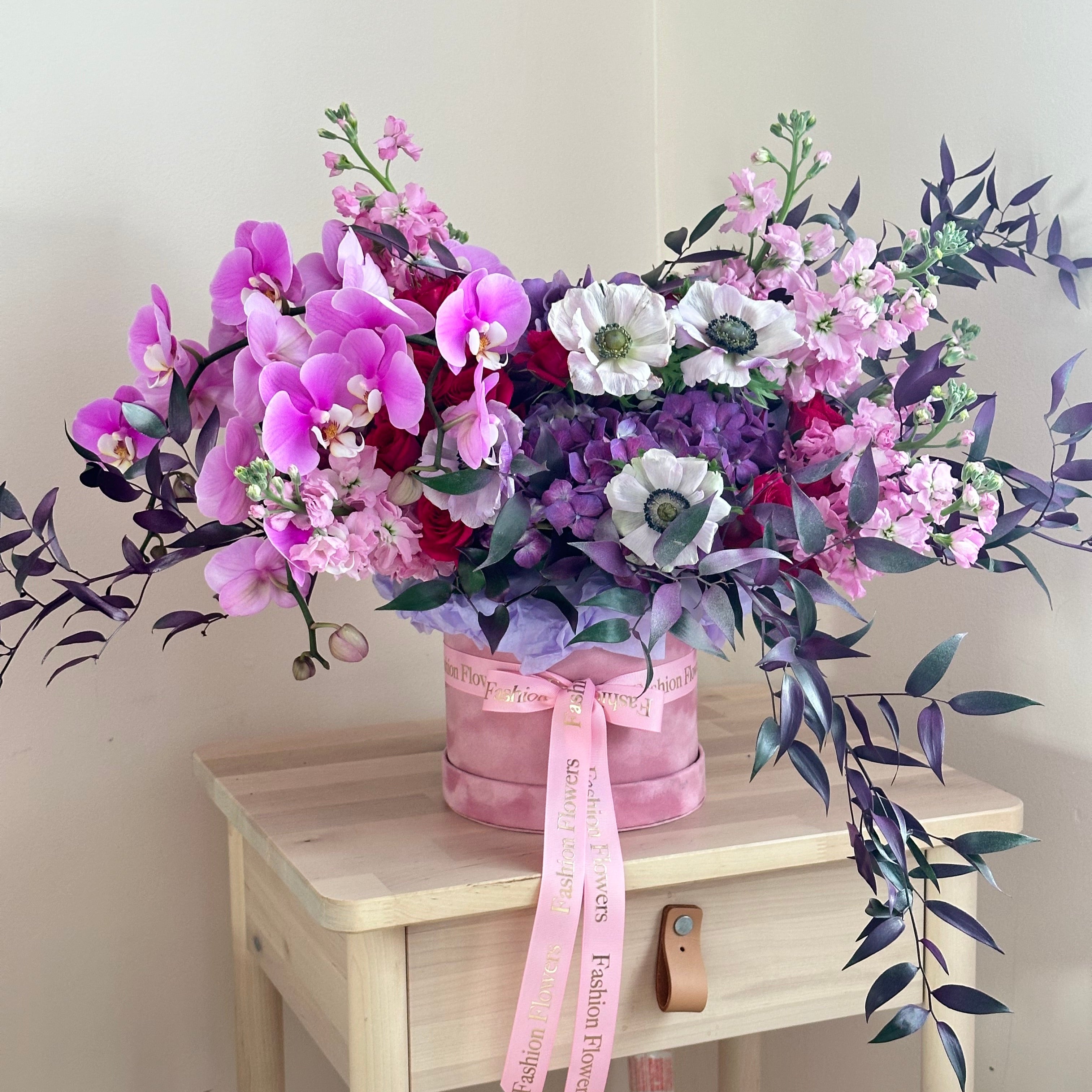Purple velvet floral bouquet with orchids and anemones in a pink designer box held on a yacht — luxury flower delivery Miami