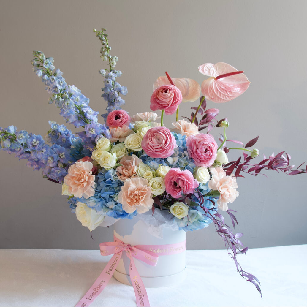 Shadows in Paradise pastel bouquet with soft roses and delphinium in white hatbox on tropical oceanfront terrace — luxury flower design Miami