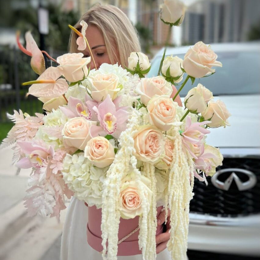 Large blush box with roses and orchids held by woman in front of villa and white car — Miami flower delivery