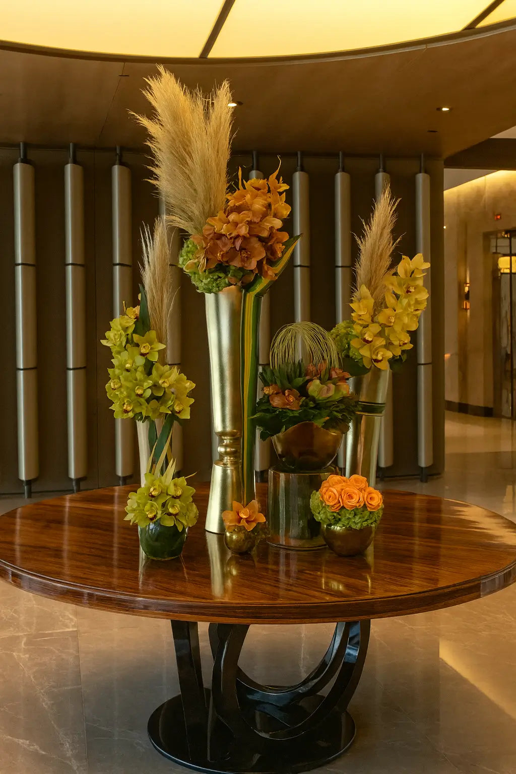 A luxurious floral arrangement in tall golden vases, featuring cascading orchids and exotic blooms, displayed on a round table in the elegant marble lobby of Fendi Château Residences.