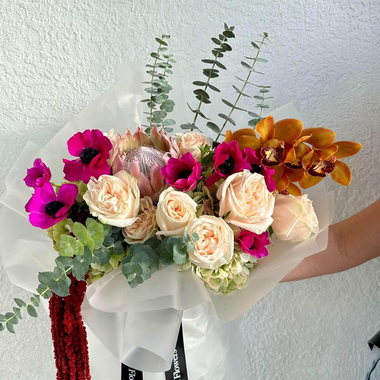 Tropical Mood hand-tied bouquet in white wrap with orchids and anemones — romantic luxury flower delivery Miami