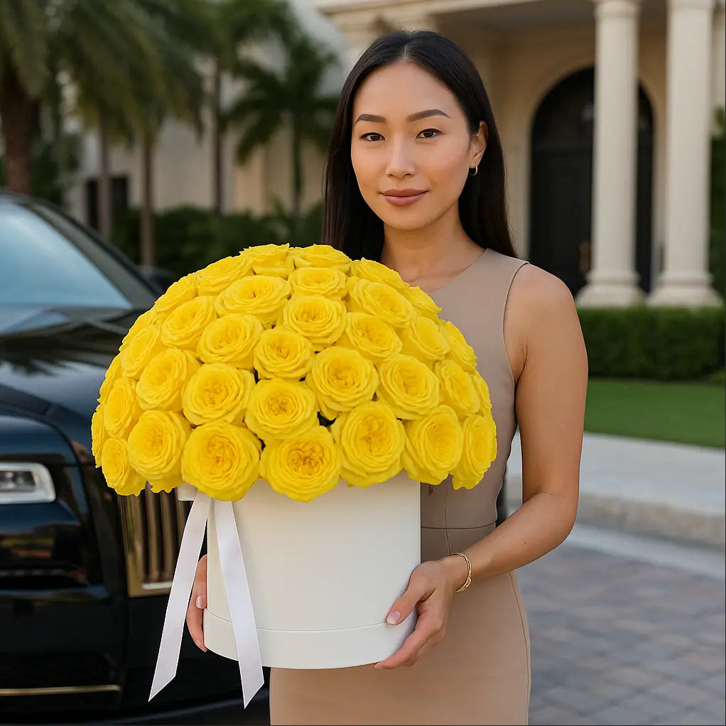 Elegant round box of yellow roses held by woman in front of Rolls-Royce and luxury villa — premium Miami flower delivery